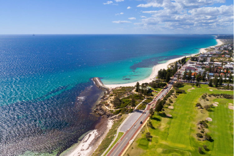 An aerial image of a gold course beside the ocean and beaches winding up the coast into the distance.